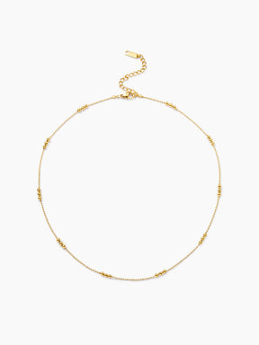 Zarte goldene Halskette im Kugel-Design, bei der sich feine Kettenglieder mit Gruppen von drei größeren, glänzenden Goldkugeln abwechseln.