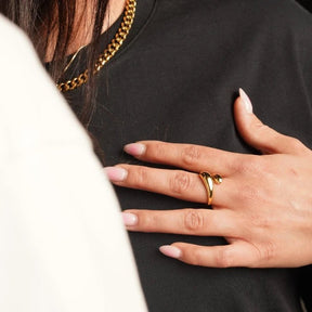 Offener Ring in Gold, dessen Enden zu dicken, geschwungenen Tropfen geformt sind, die an der Oberseite aneinander vorbeigleiten.