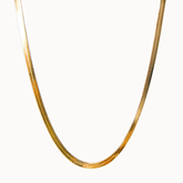 Breite, flach aufliegende Goldkette mit feiner Struktur, die wie eine flüssige goldene Linie wirkt.