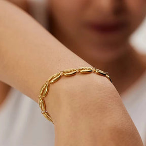 Armband aus aneinandergereihten, gold-glänzenden Kaurimuscheln mit verstellbarem Verschlusskettchen.