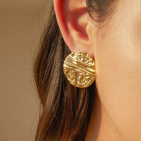 Große goldene Statement-Ohrstecker mit unregelmäßiger, gehämmerter Oberfläche und organischem Relief-Design.