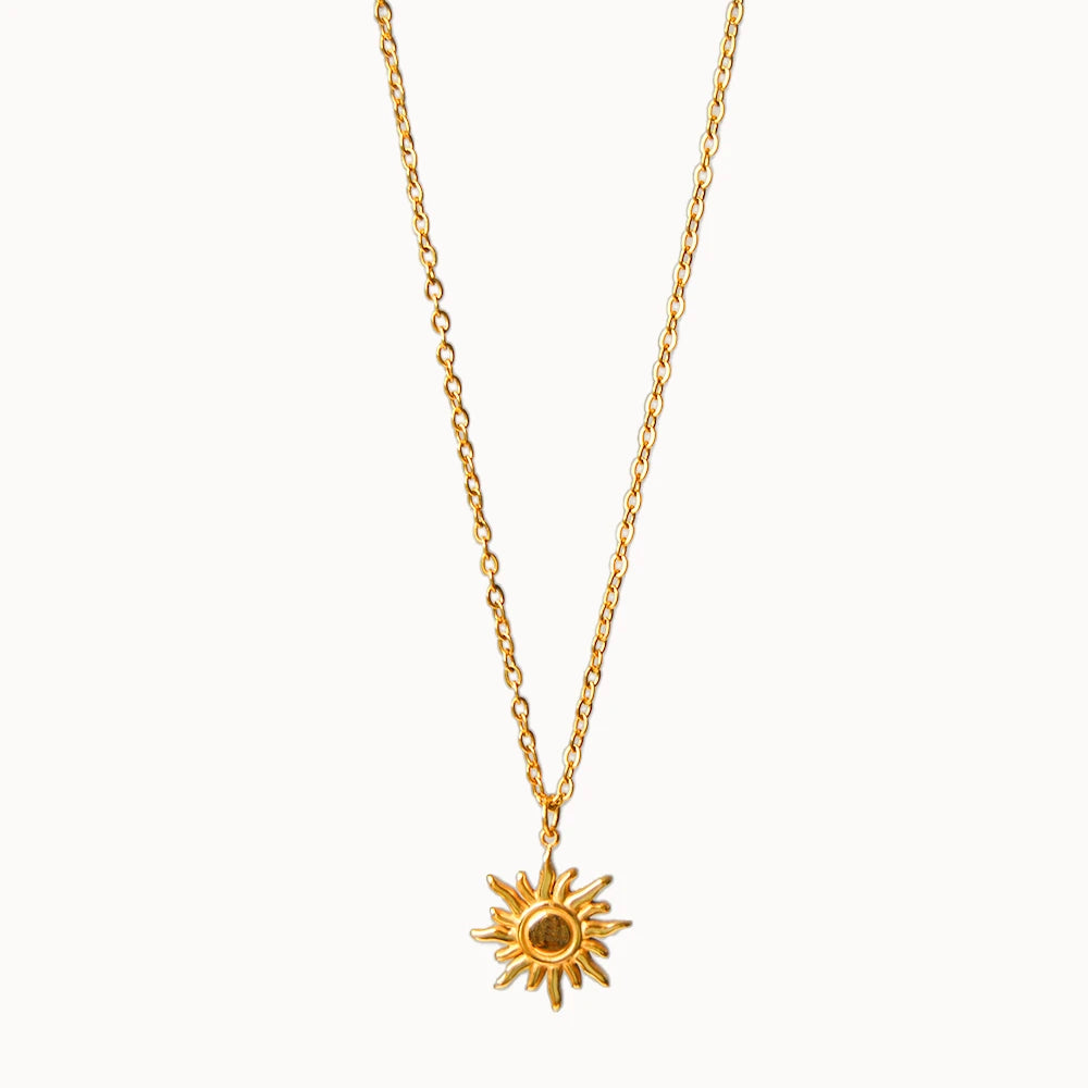 Feine Gliederkette in Gold, an der ein runder Anhänger in Form einer Sonne mit geschwungenen Strahlen hängt.