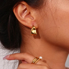 Elegante Creolen in Gold mit einer modernen, skulpturalen Silhouette und fließender Metall-Optik.