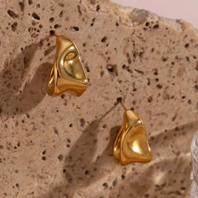 Elegante Creolen in Gold mit einer modernen, skulpturalen Silhouette und fließender Metall-Optik.