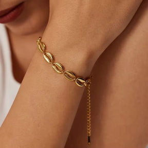 Armband aus aneinandergereihten, gold-glänzenden Kaurimuscheln mit verstellbarem Verschlusskettchen.