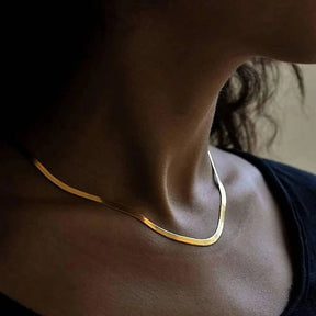 Breite, flach aufliegende Goldkette mit feiner Struktur, die wie eine flüssige goldene Linie wirkt.