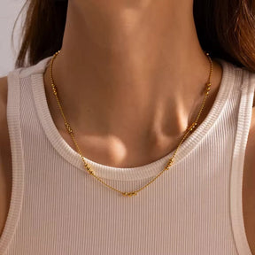 Zarte goldene Halskette im Kugel-Design, bei der sich feine Kettenglieder mit Gruppen von drei größeren, glänzenden Goldkugeln abwechseln.
