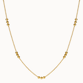 Zarte goldene Halskette im Kugel-Design, bei der sich feine Kettenglieder mit Gruppen von drei größeren, glänzenden Goldkugeln abwechseln.