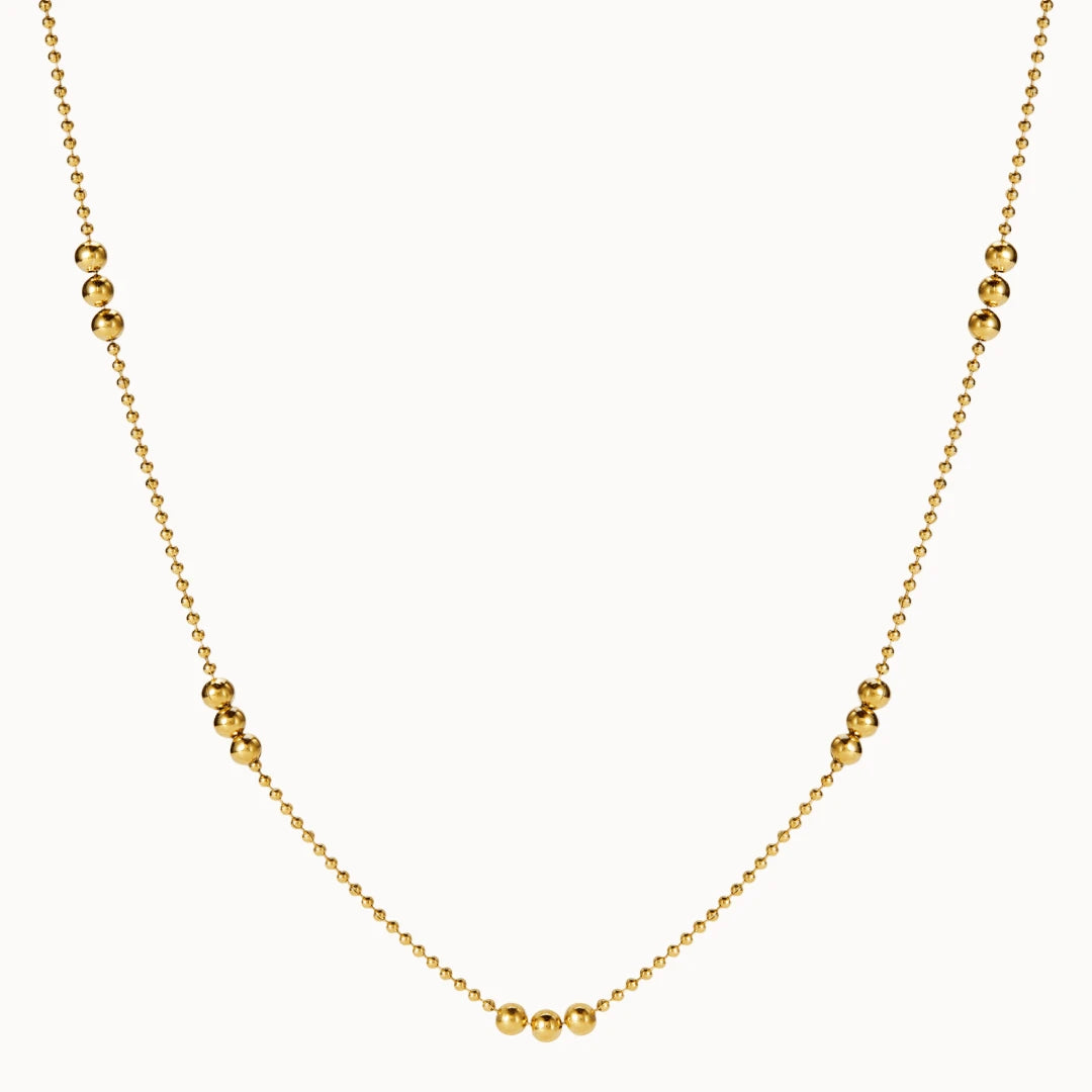 Zarte goldene Halskette im Kugel-Design, bei der sich feine Kettenglieder mit Gruppen von drei größeren, glänzenden Goldkugeln abwechseln.