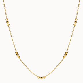 Zarte goldene Halskette im Kugel-Design, bei der sich feine Kettenglieder mit Gruppen von drei größeren, glänzenden Goldkugeln abwechseln.