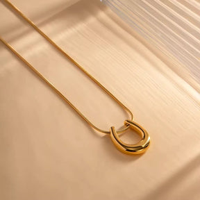 Feine Halskette in Gold, an der ein glänzender, gebogener Loop-Anhänger gleitet.